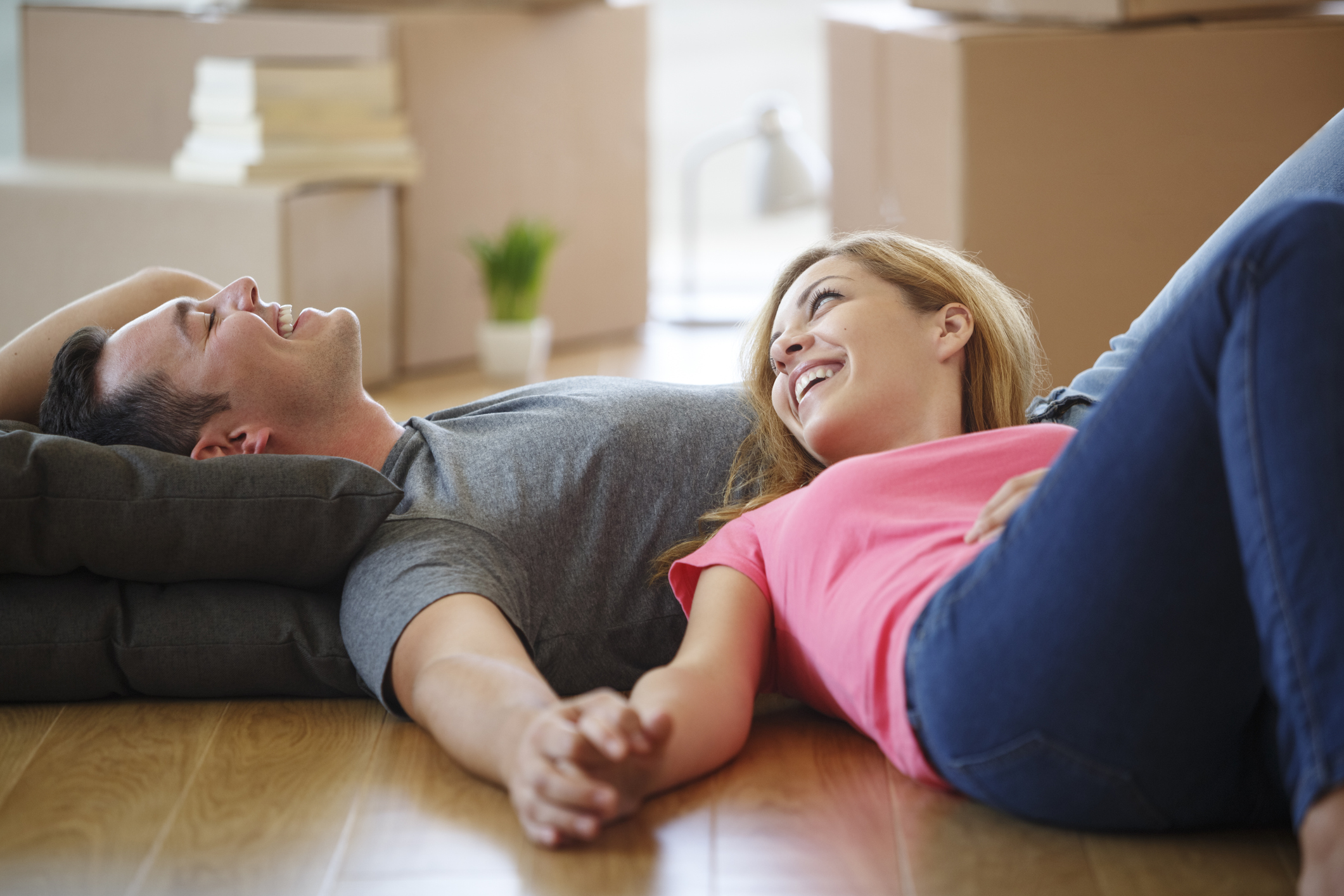 Junges Paar liegt erschöpft und lächelnd auf dem Fußboden der neuen Wohnung.